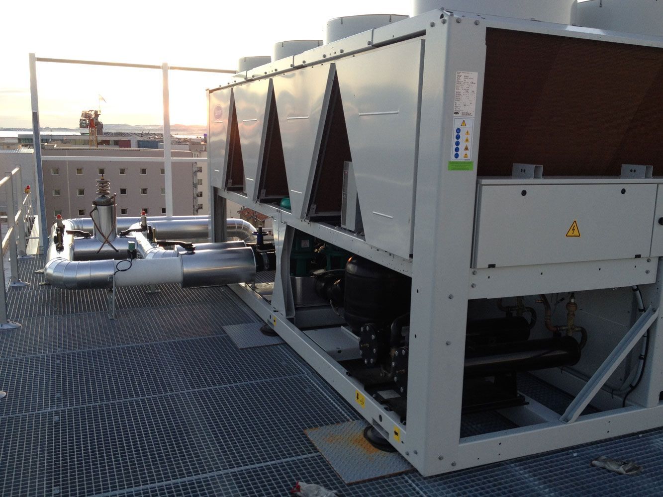 Unité de refroidissement de grande taille sur le toit, avec tuyaux métalliques, conduits d'aération et plateforme en grille métallique.