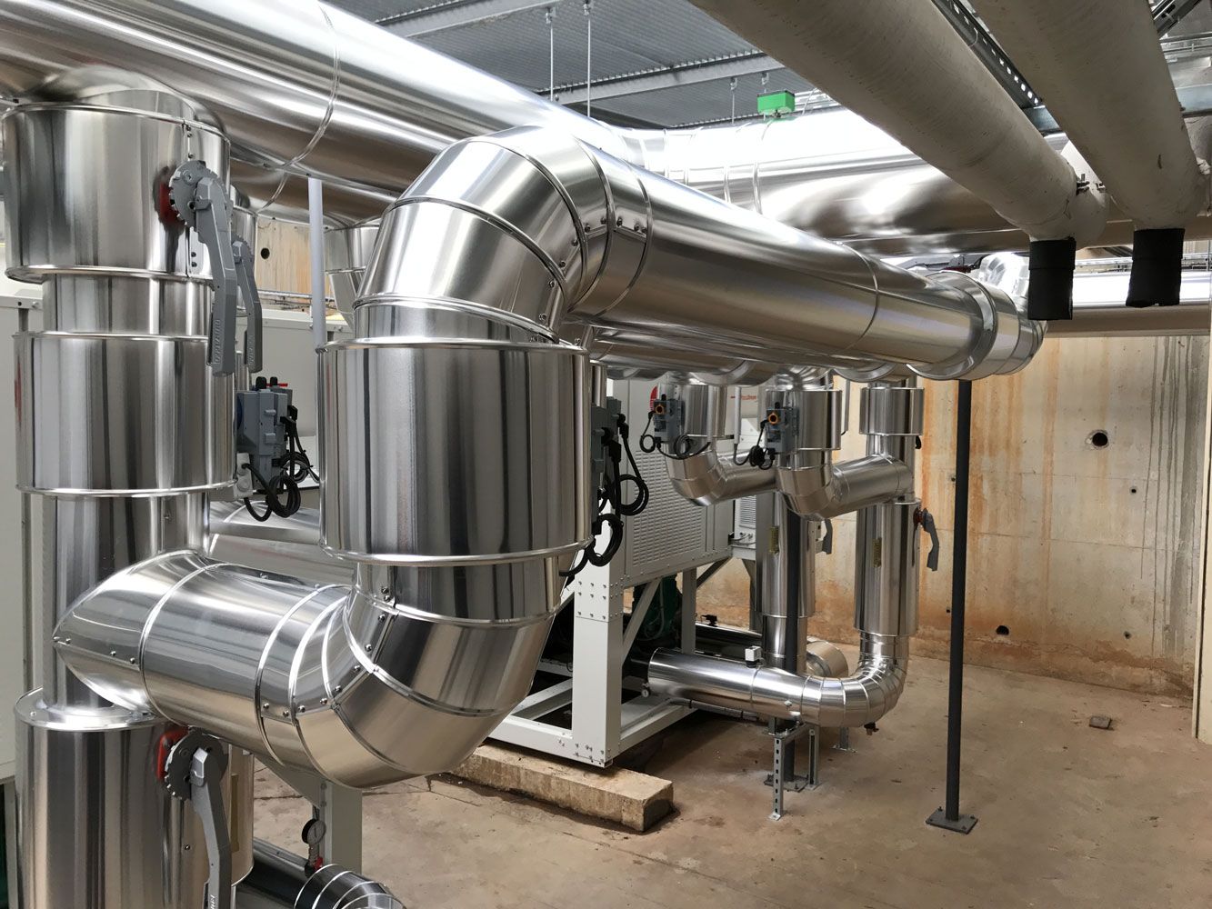 Tuyaux isolés à revêtement argenté et vannes dans un environnement industriel.