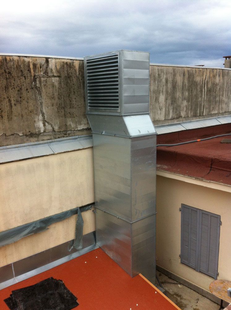 Un conduit de ventilation métallique rectangulaire s'élève d'un coin de toit ; ciel gris et nuageux au-dessus.