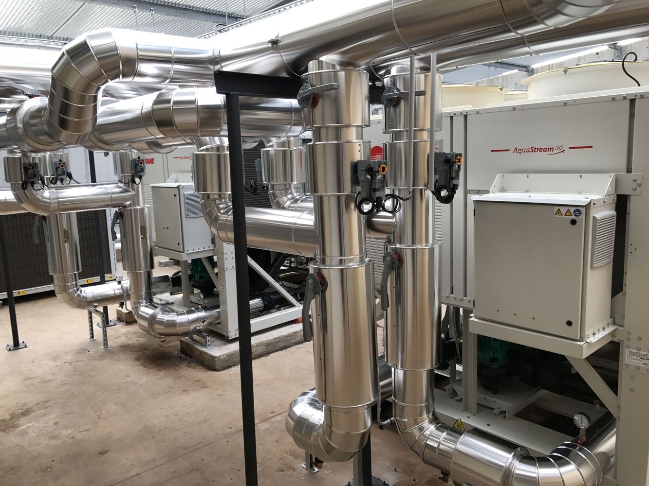 Tuyauteries et machines industrielles dans un local technique, comprenant des tuyaux métalliques isolés et des panneaux de commande.