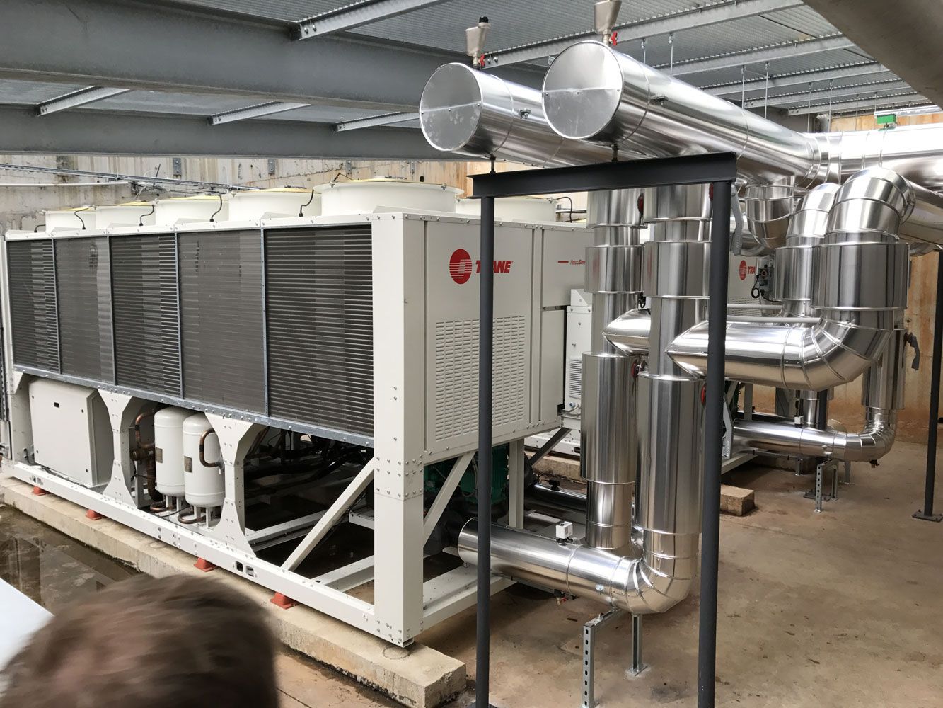 Unité de climatisation industrielle de grande taille avec tuyauterie argentée dans un local technique.