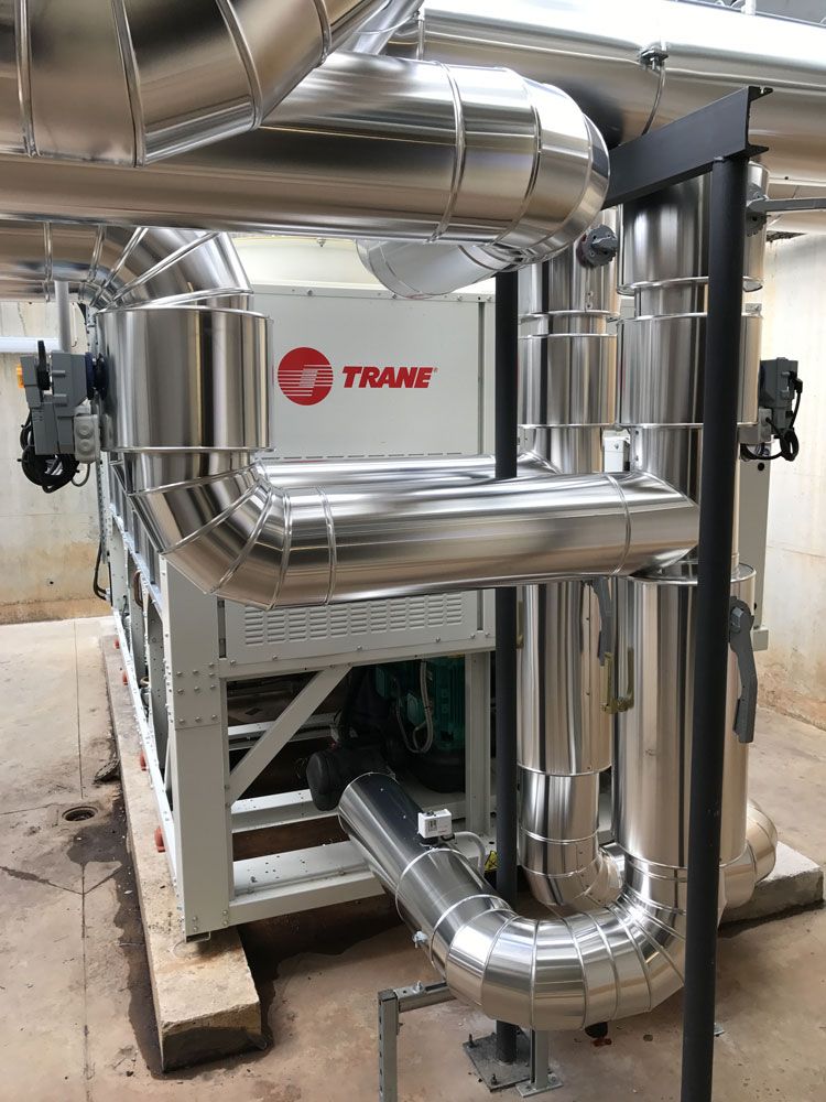 Un groupe frigorifique Trane avec des tuyaux argentés isolés, dans un environnement industriel.