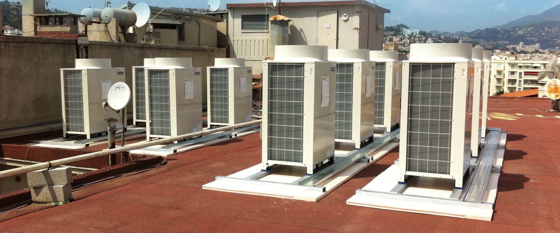 Unités de climatisation sur un toit, avec une ville et des collines en arrière-plan.