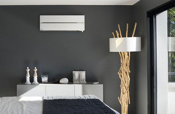Chambre moderne avec mur gris, climatiseur, lampe et lit blanc et gris.