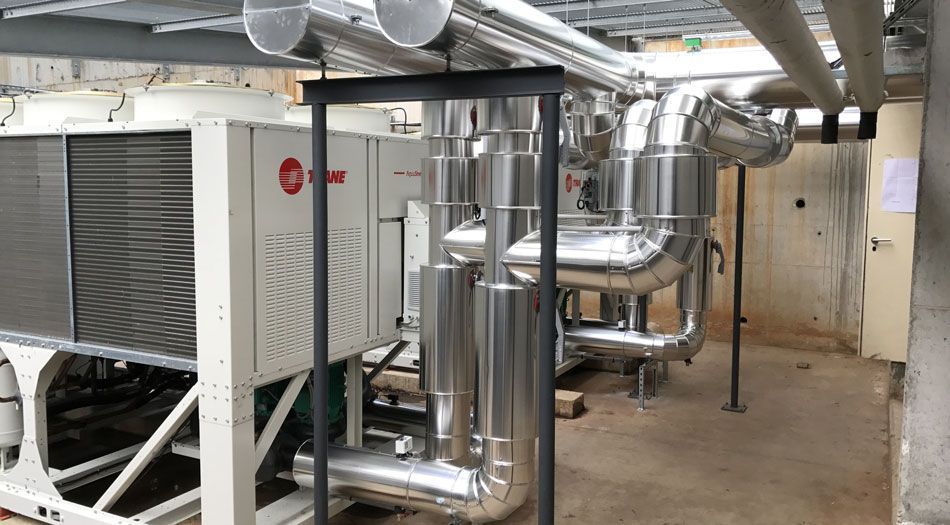 Équipement de climatisation avec tuyauterie en milieu industriel. Unité blanche avec ventilateur et tuyauterie métallique apparente.