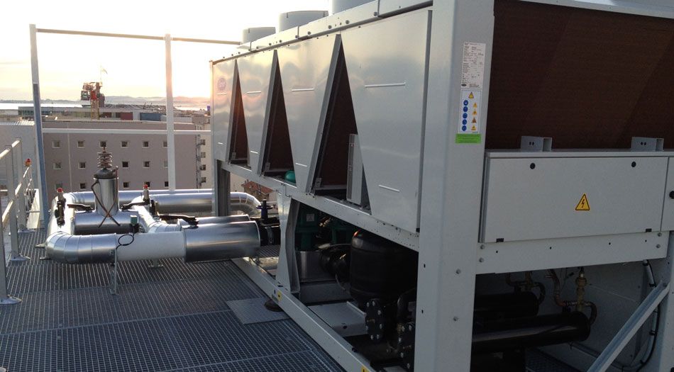 Un grand refroidisseur industriel installé sur un toit, avec des tuyaux et des structures métalliques. Le ciel est visible en arrière-plan.