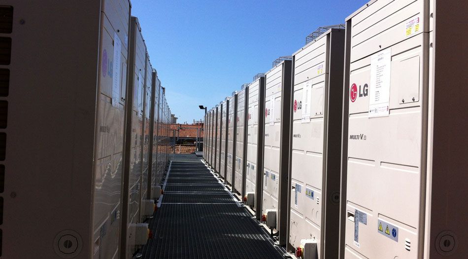 Des rangées d'unités de climatisation industrielles sur un toit, séparées par une passerelle métallique.