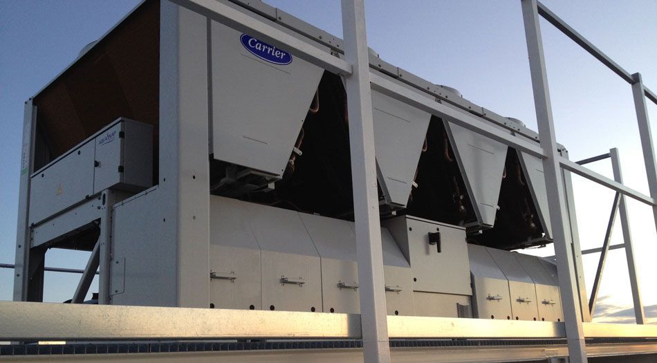 Unité de climatisation industrielle de grande taille installée sur un toit, avec des bouches d'aération et une structure métallique, en plein soleil.