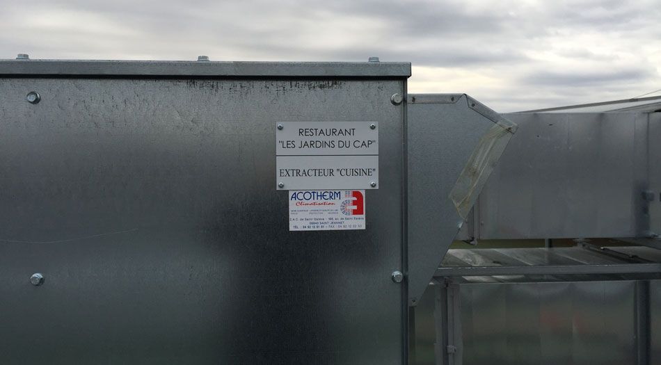 Unité de climatisation métallique avec une étiquette sur fond de ciel nuageux.