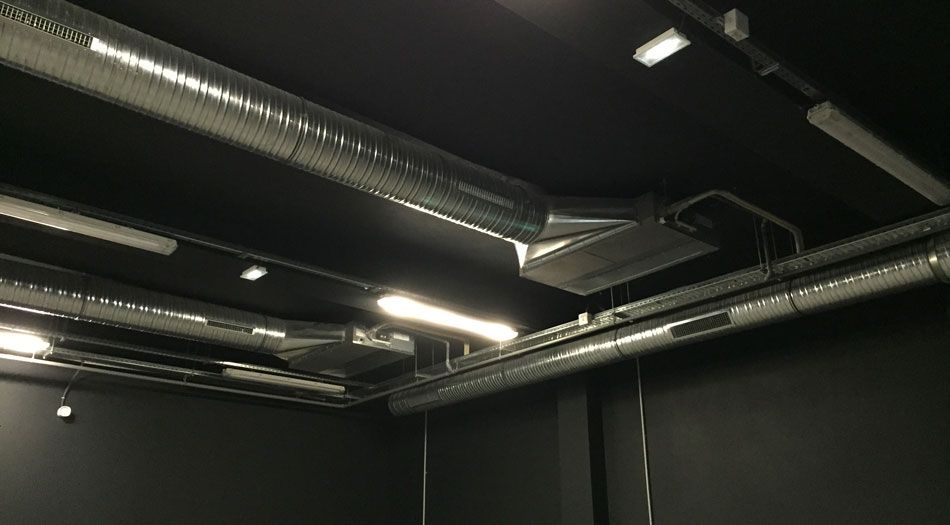 Plafond noir avec conduits de ventilation argentés et éclairage fluorescent.