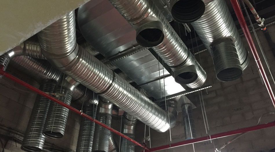 Conduits de ventilation métalliques au plafond, avec un tuyau rouge longeant le tout.