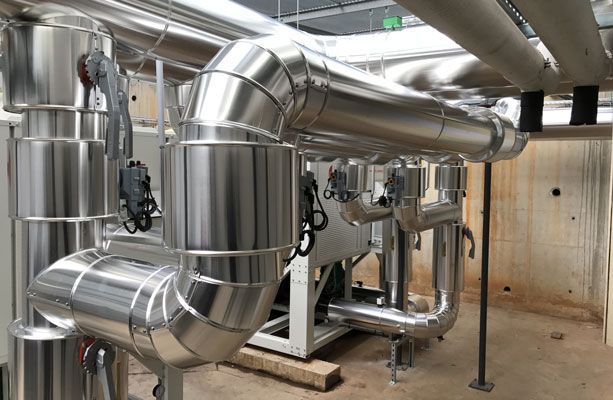 Tuyaux métalliques isolés en milieu industriel, avec vannes et revêtement argenté.