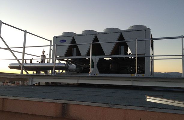 Unité de climatisation sur le toit avec garde-corps, se détachant sur un ciel de coucher de soleil.