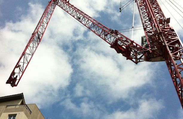 Grue de chantier rouge se détachant sur un ciel bleu nuageux, dominant un bâtiment.