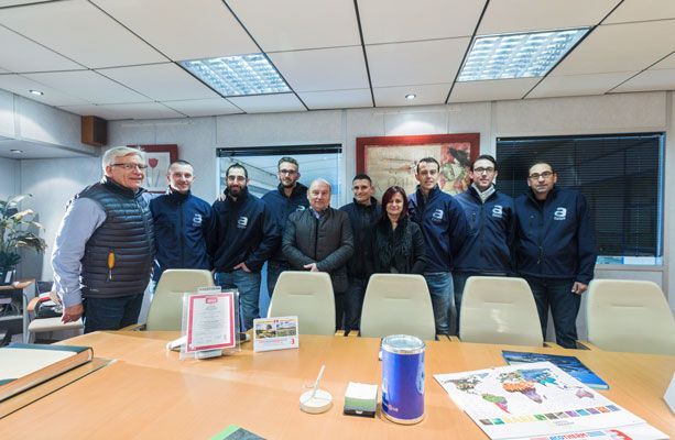 Un groupe de personnes se tient derrière une table de conférence dans un bureau. Elles regardent la caméra.