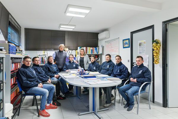 Un groupe de personnes en vestes bleues est assis autour d'une table dans un bureau baigné de lumière.