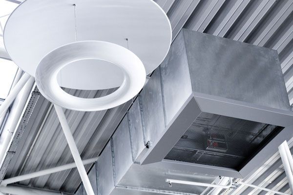 Conduits de ventilation industriels gris et luminaires décoratifs circulaires au plafond.