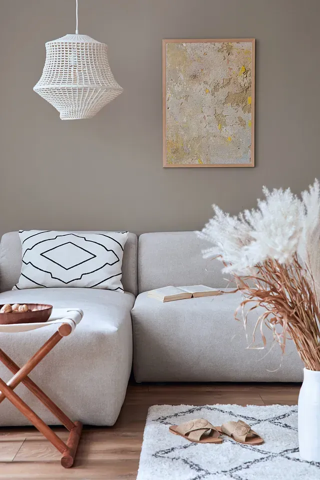 Acogedora sala de estar con sofá claro, lámpara tejida, arte abstracto, hierba de la pampa y una pequeña mesa auxiliar de madera.