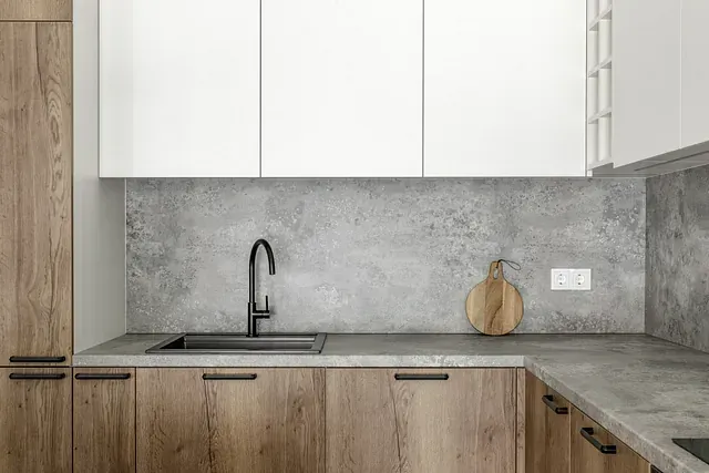 Cocina moderna con gabinetes de madera, salpicadero y encimeras de hormigón y grifo negro.