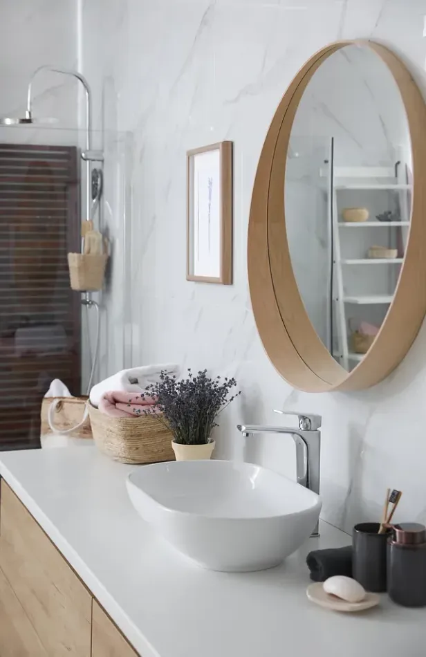 Baño con lavabo blanco, espejo y accesorios; toallas y flores en la encimera.