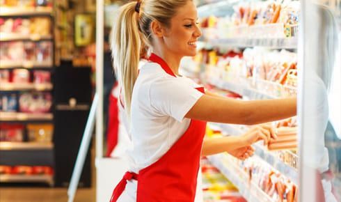 Femme en tablier rouge rangeant un frigo au supermarché