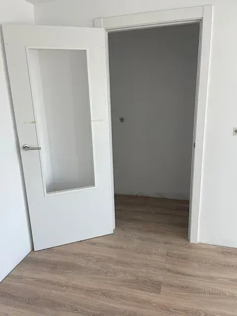 Una habitación vacía con una puerta blanca y un piso de madera.
