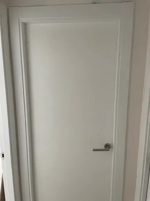 Una puerta blanca con tirador en un pasillo.
