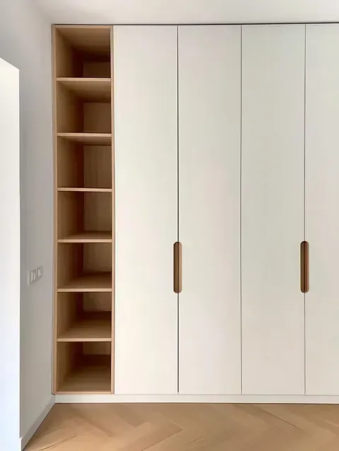 Un dormitorio con armarios blancos y estantes de madera.