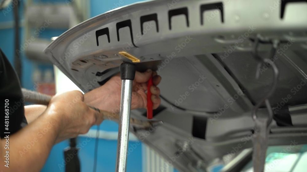 Person, die mit einem Werkzeug die Unterseite einer grauen Autostossstange repariert
