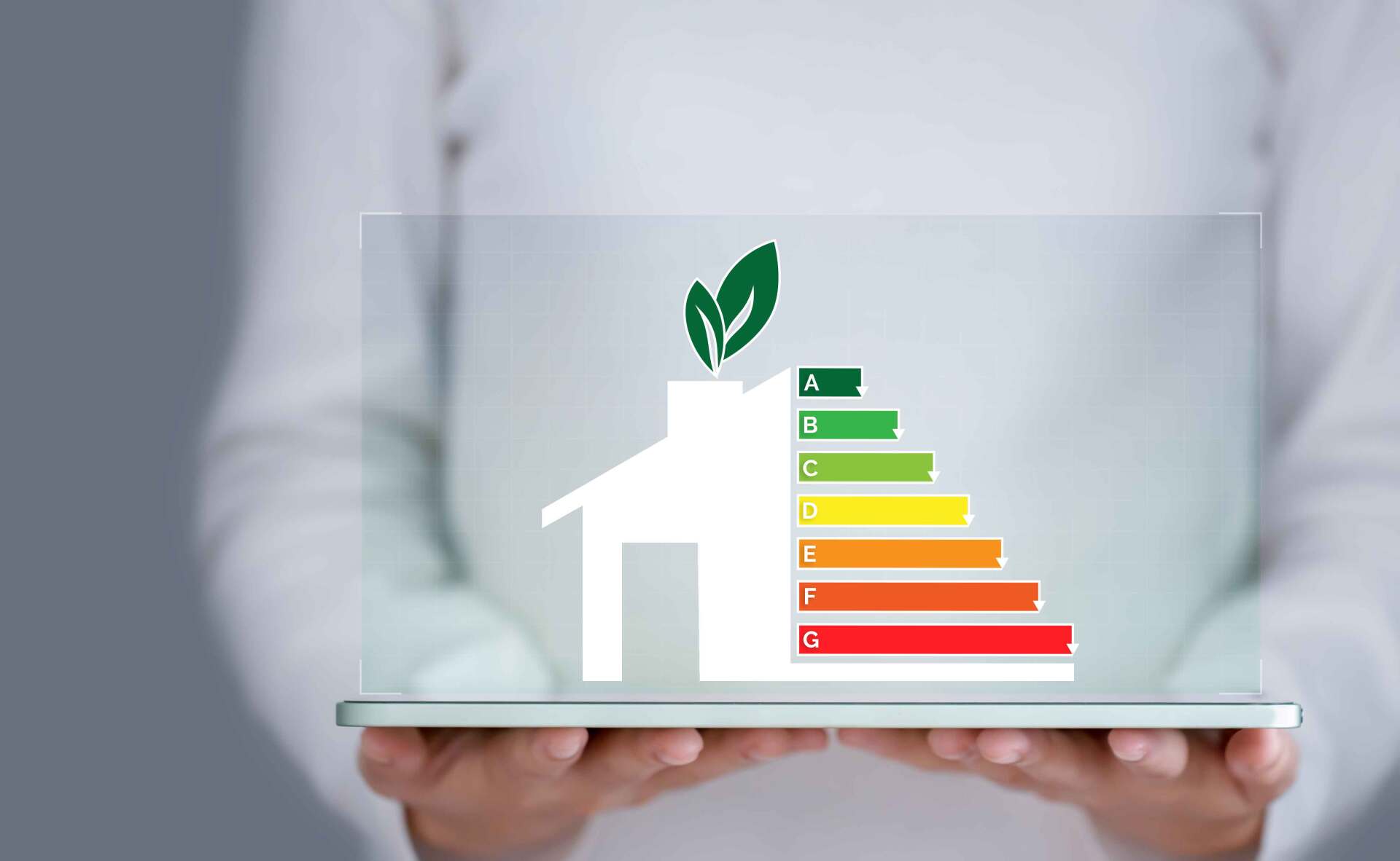 Une personne tenant une plaque transparente avec dessus un diagramme représentant une maison et les 7 différents niveaux de consommation d'énergie colorés du vert au rouge