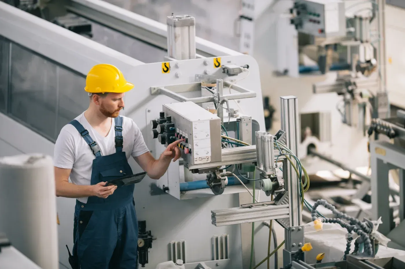 Ein Arbeiter mit gelbem Schutzhelm inspiziert Maschinen auf einer Fabrikfläche.