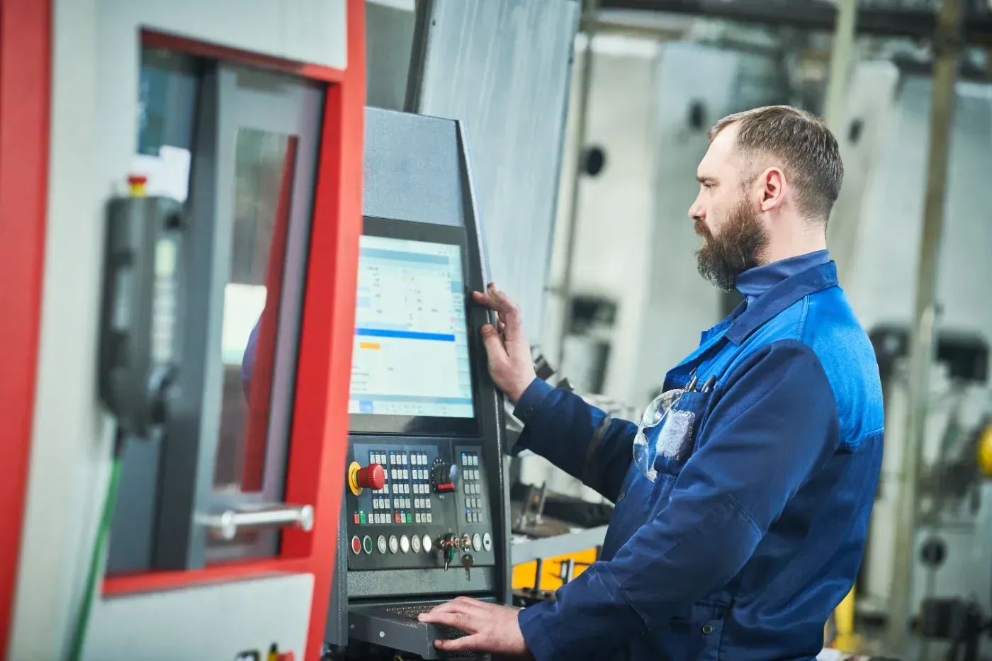 Ein Arbeiter in blauer Arbeitskleidung bedient eine Fabrikmaschine mit Touchscreen-Bedienfeld.