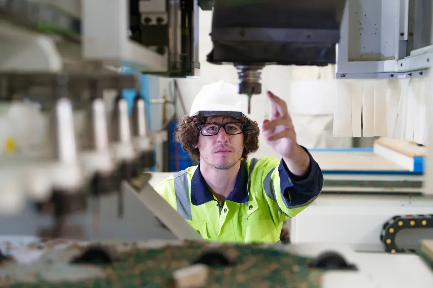 Ein Arbeiter mit Schutzhelm und Sicherheitsweste inspiziert Maschinen in einer Fabrik.