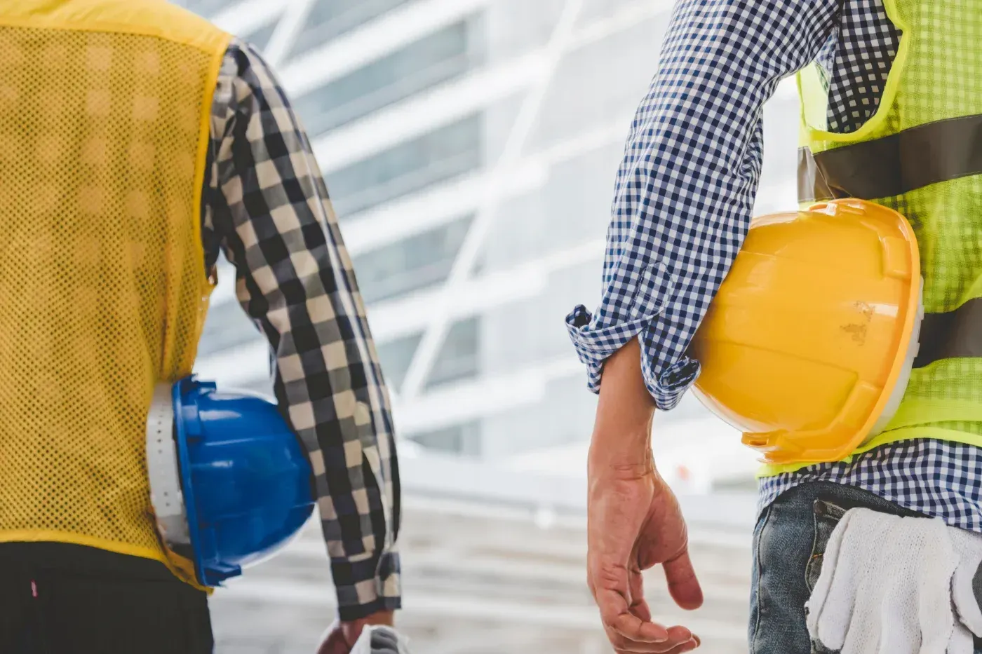 Zwei Bauarbeiter in Sicherheitswesten halten blaue und gelbe Schutzhelme auf einer Baustelle