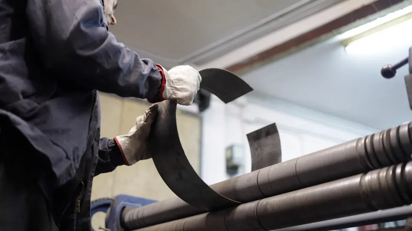 Ein Arbeiter mit Handschuhen hantiert in einer Industriehalle mit einem schwarzen Streifen an einer Maschine.