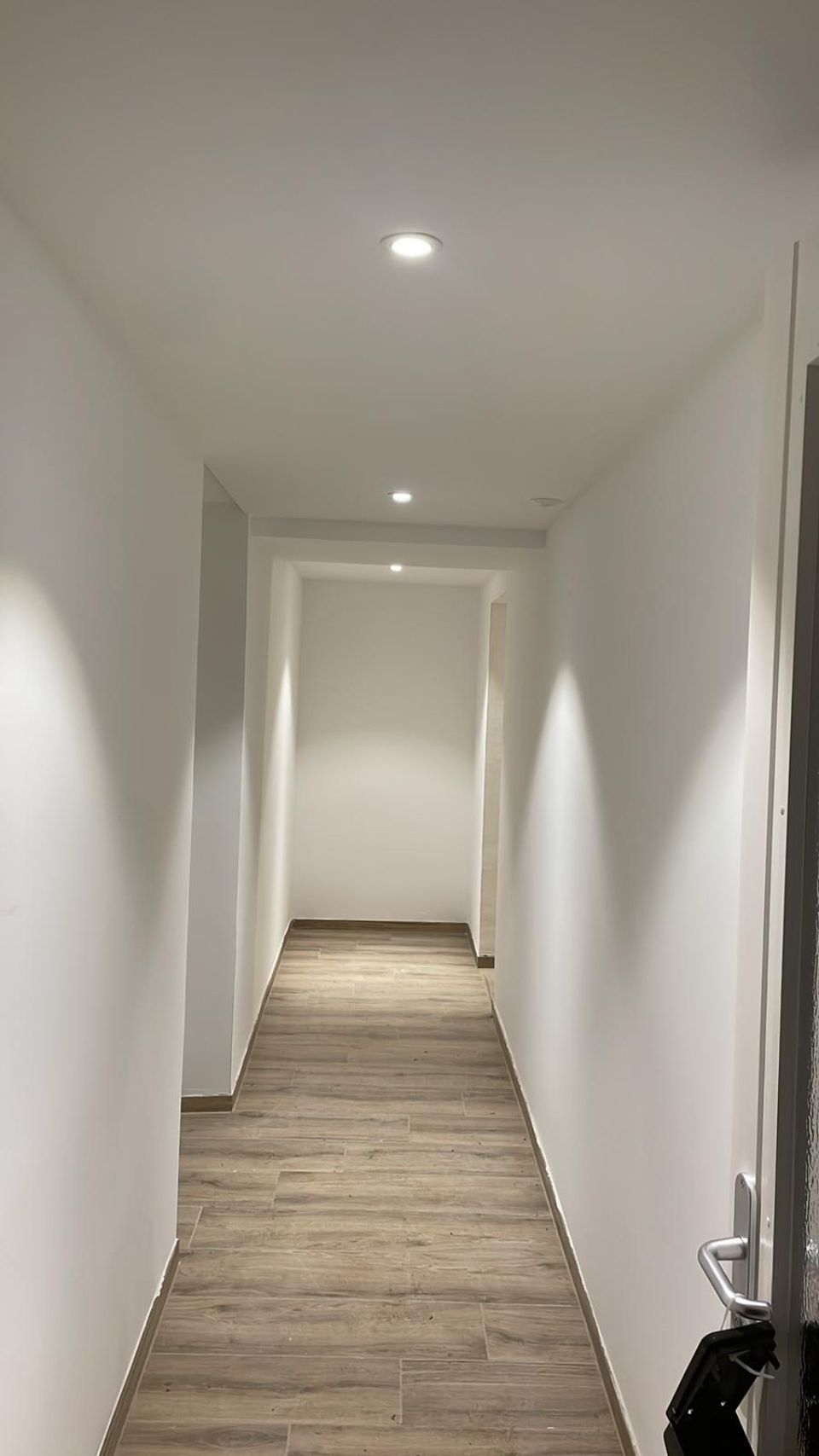 Un lungo corridoio con pavimenti in legno e pareti bianche.