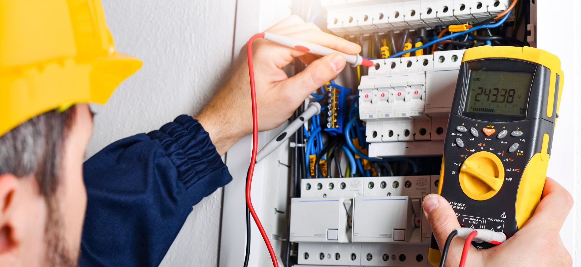 Un électricien teste un tableau de disjoncteurs avec un multimètre dans une buanderie.