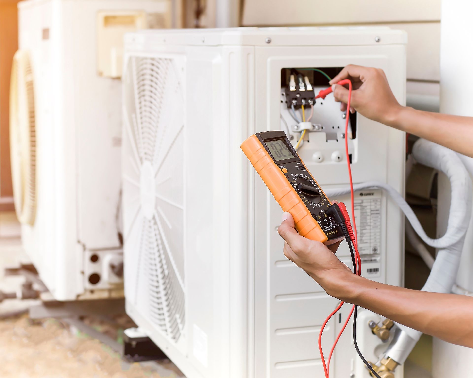 Un technicien teste une unité de climatisation extérieure à l'aide d'un multimètre et de sondes.