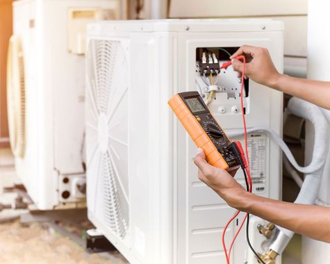 Un technicien teste une unité de climatisation extérieure à l'aide d'un multimètre et de sondes.