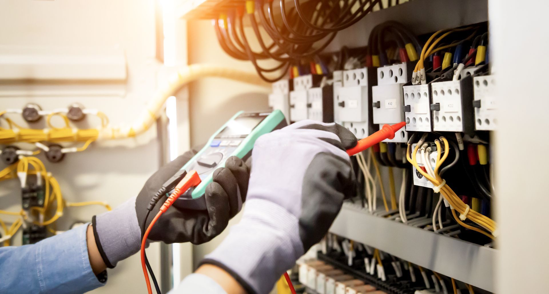 Un électricien teste le câblage d'un tableau électrique à l'aide d'un multimètre et d'un tournevis.