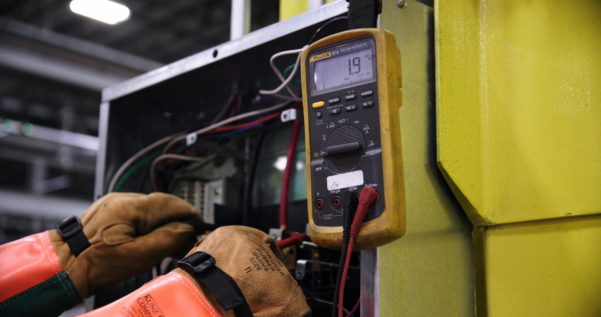 Des mains utilisent un multimètre numérique pour tester le câblage à l'intérieur d'une armoire électrique.