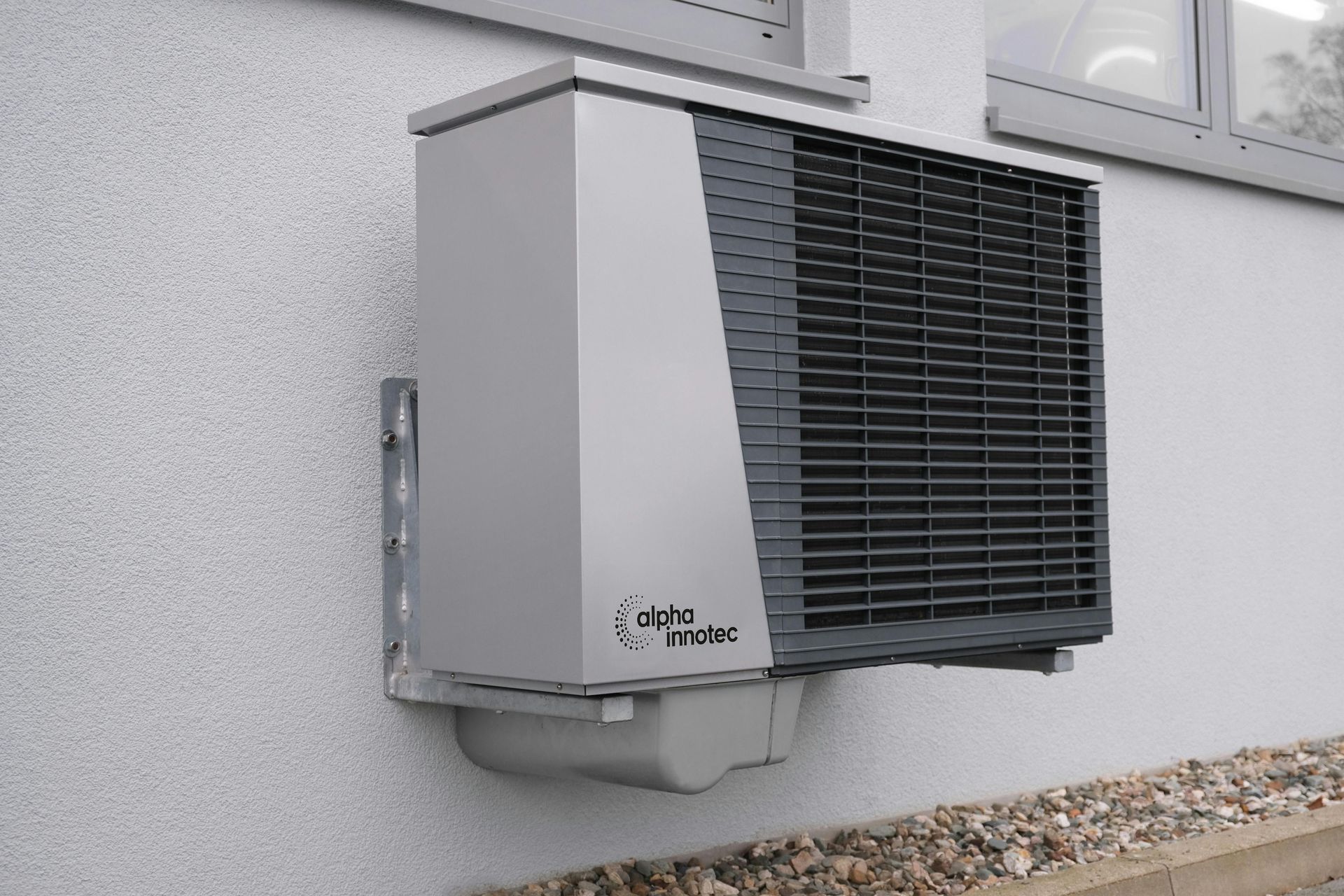 Unité de climatisation murale extérieure avec boîtier gris et grilles d'aération noires, fixée à l'extérieur d'un bâtiment.