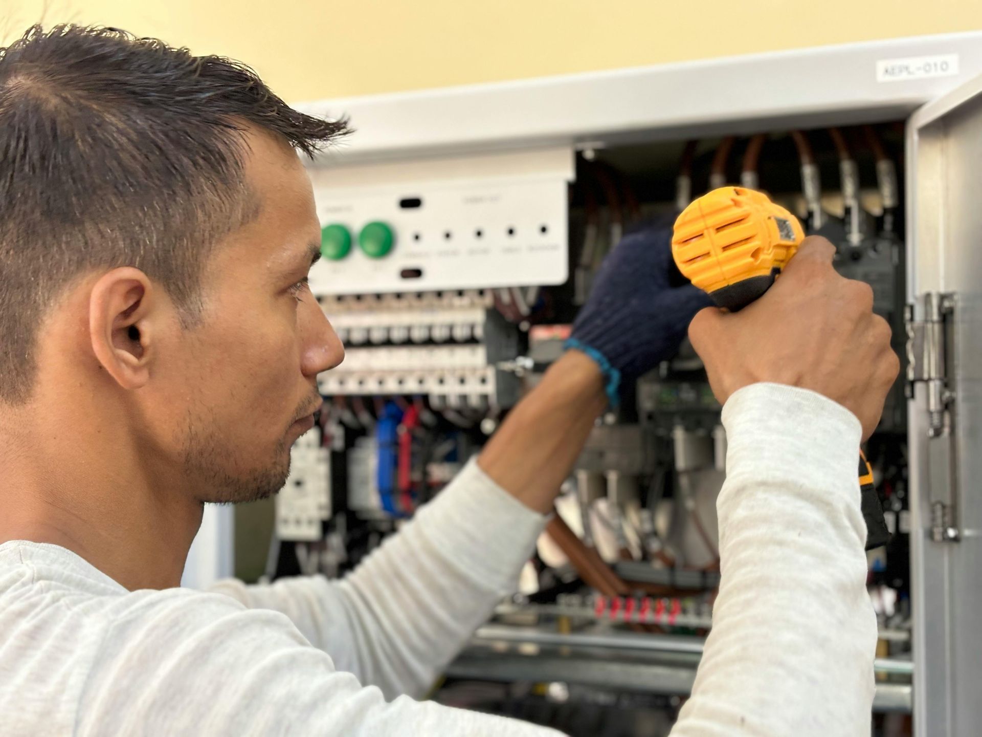 Un technicien inspecte le câblage électrique à l'intérieur d'un panneau de commande ouvert, tenant un outil jaune.