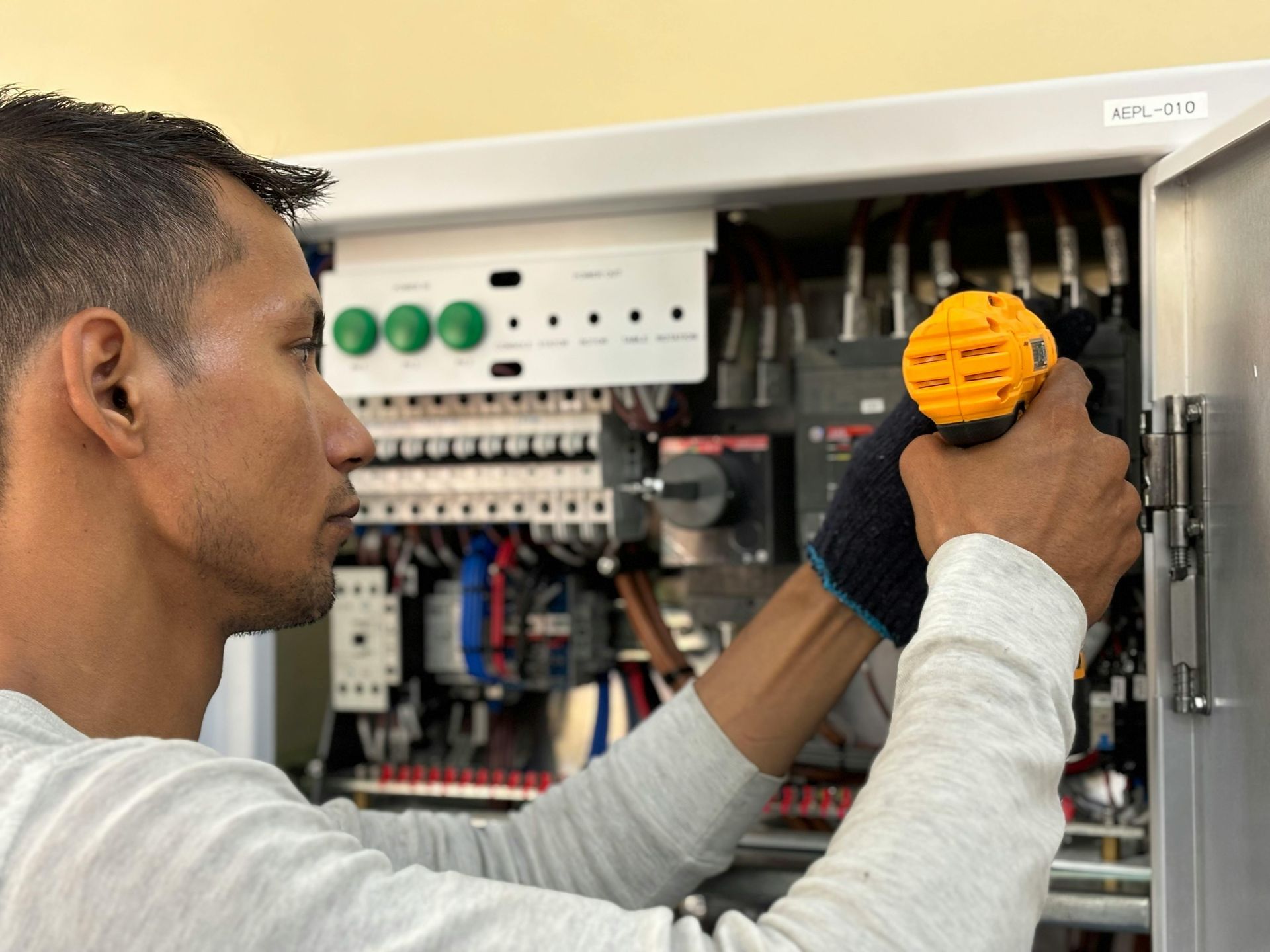 Un technicien utilise un tournevis jaune pour réparer un panneau de commande électrique ouvert.