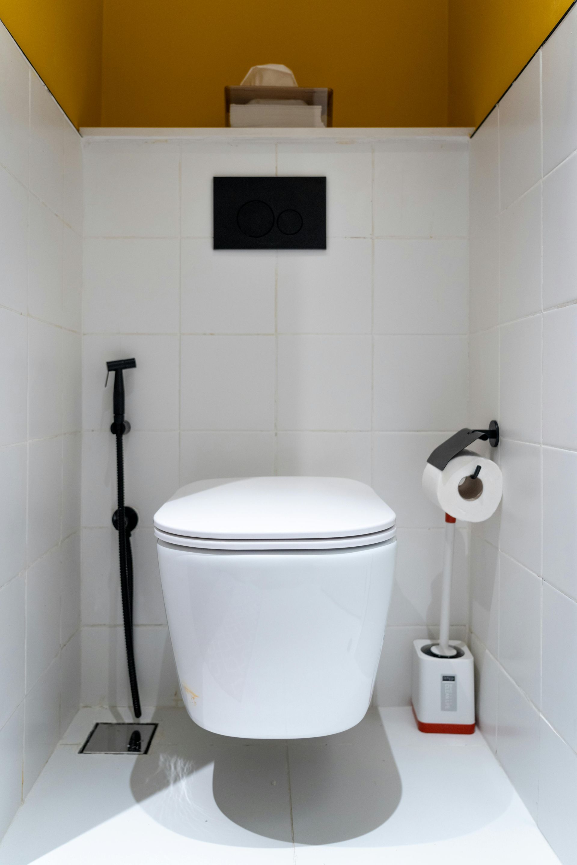 Petite salle de toilettes moderne avec WC suspendu, brosse de toilette et porte-papier toilette.