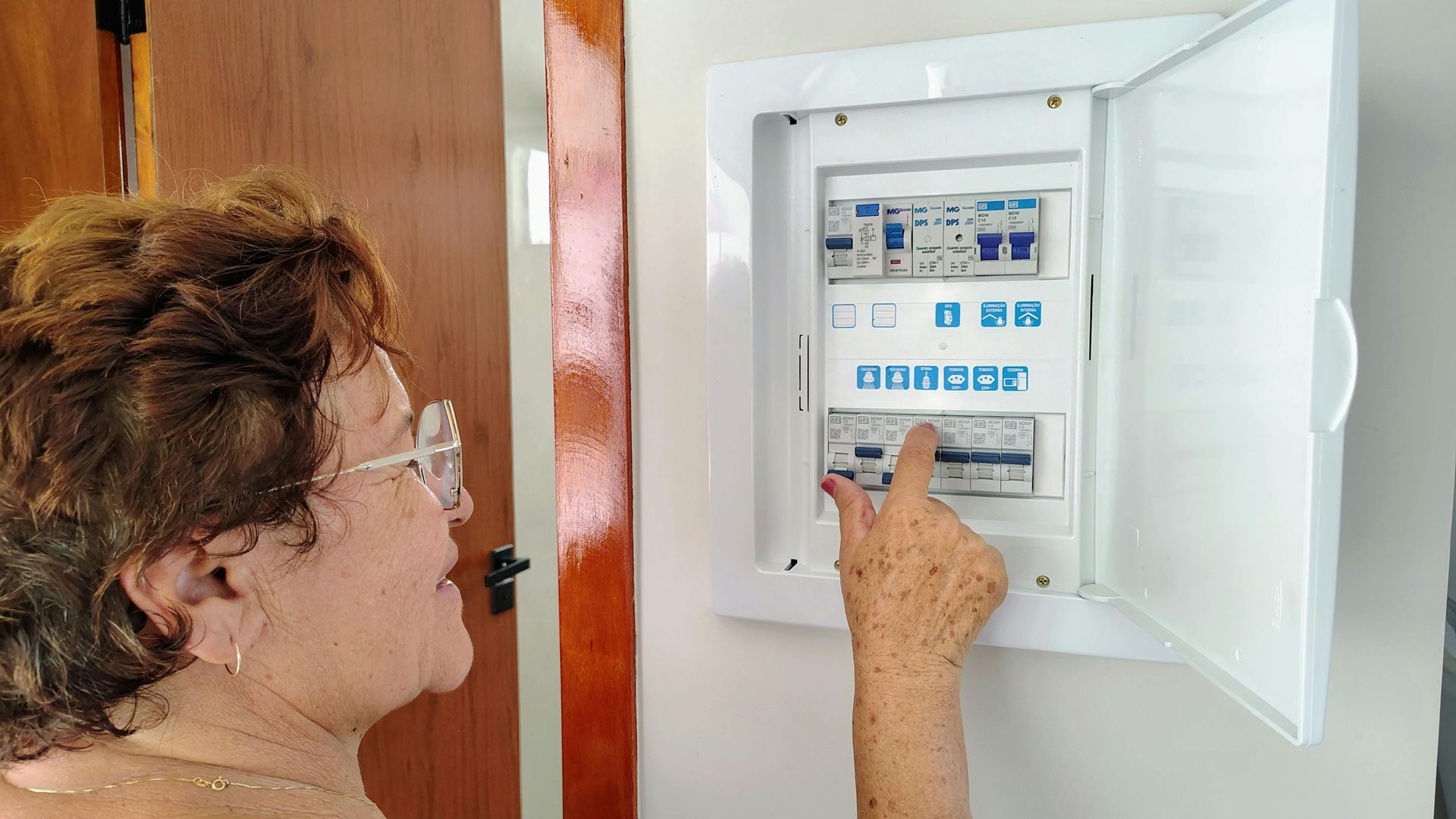Une femme ajuste un tableau de disjoncteurs dans un boîtier électrique mural.