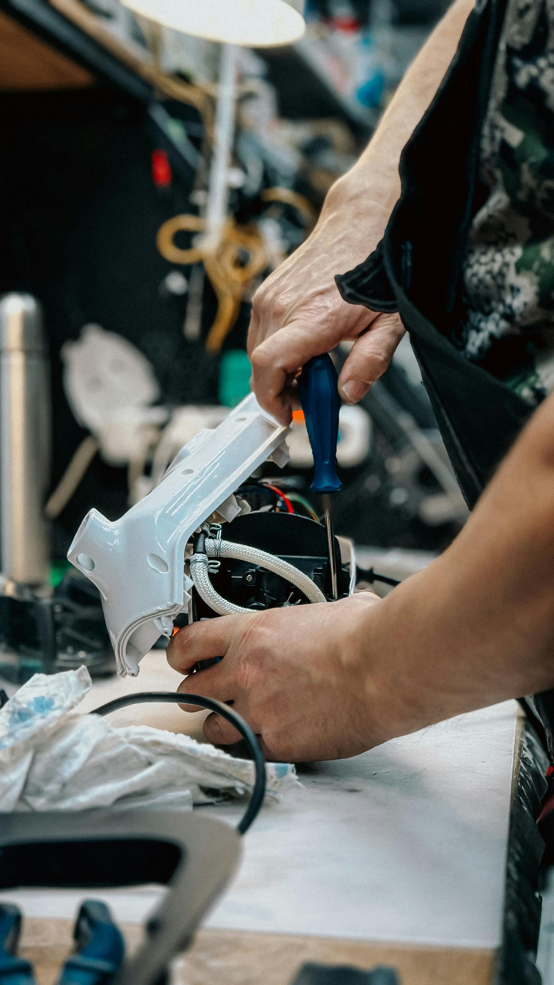 Des mains manipulent un appareil électronique blanc avec des fils sur un établi.