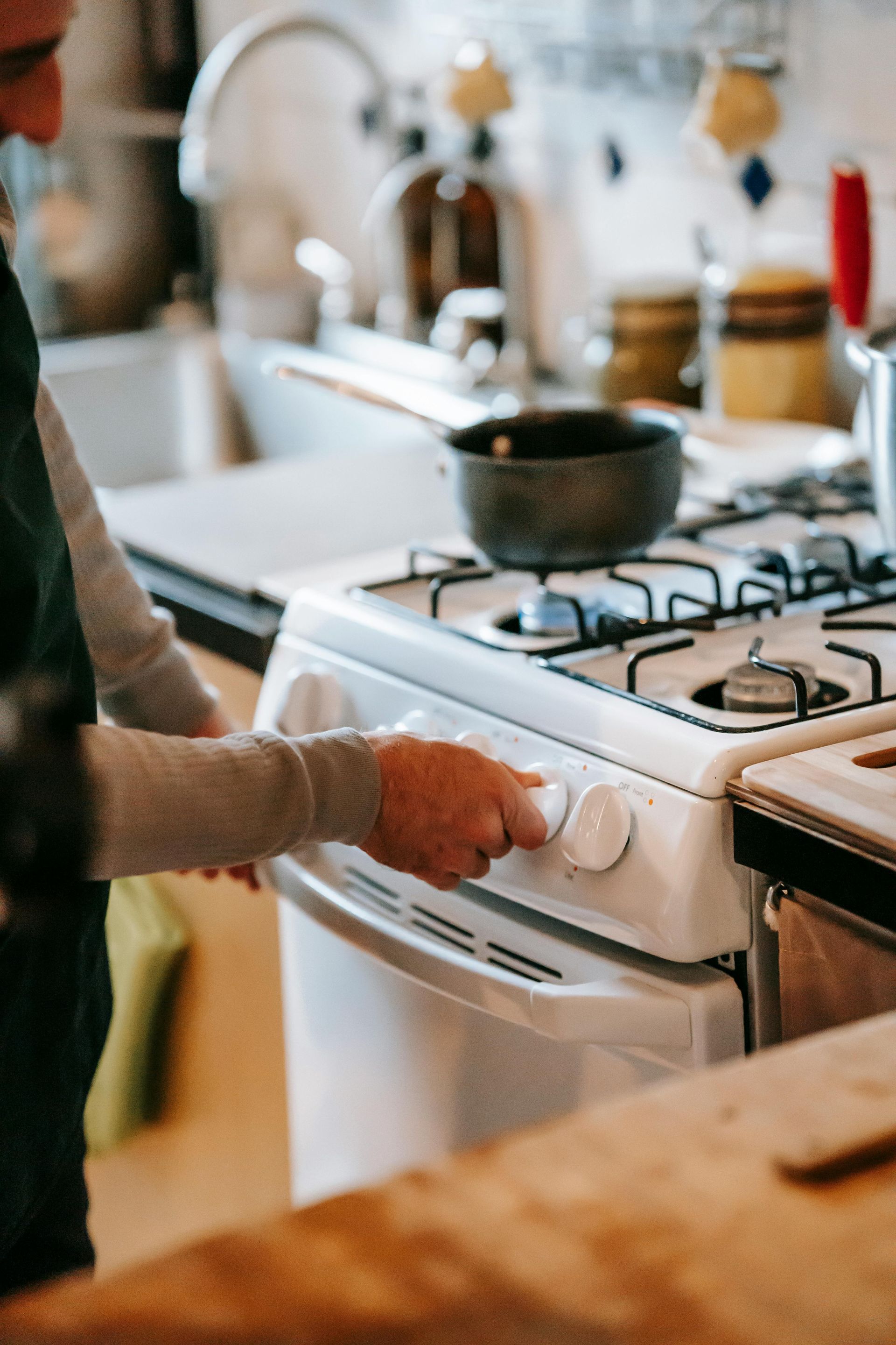 Une personne ajuste un bouton blanc de cuisinière tout en cuisinant sur une plaque de cuisson à gaz.