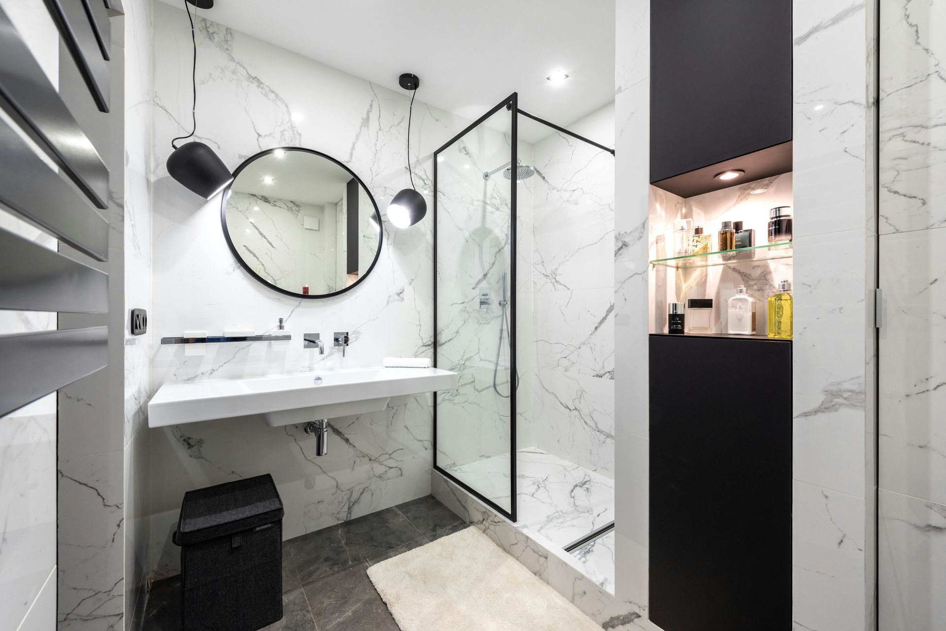 Salle de bains moderne en marbre avec miroir rond, lavabo suspendu, douche en verre et robinetterie noire.