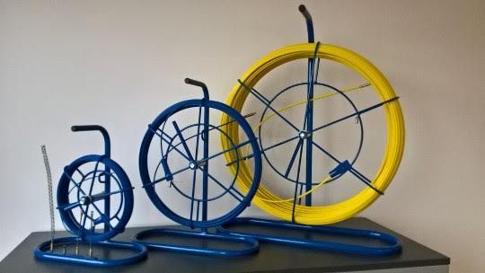 Trois outils de tirage de fils de tailles différentes, de couleur bleue, tenant des fils jaunes et gris, sur une surface noire.